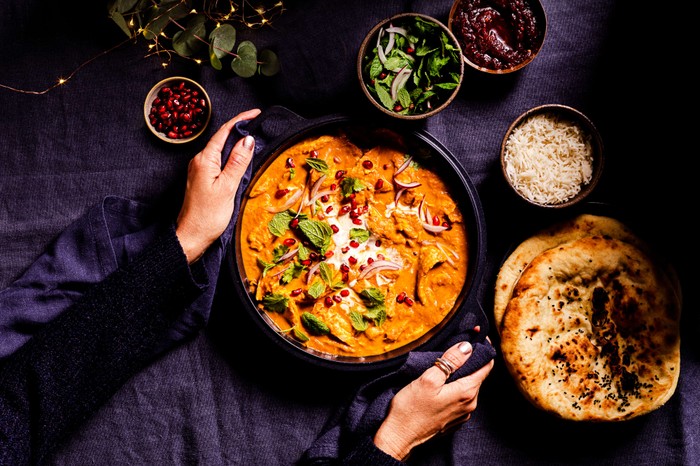 Someone setting a pan of butter turkey curry onto a set table