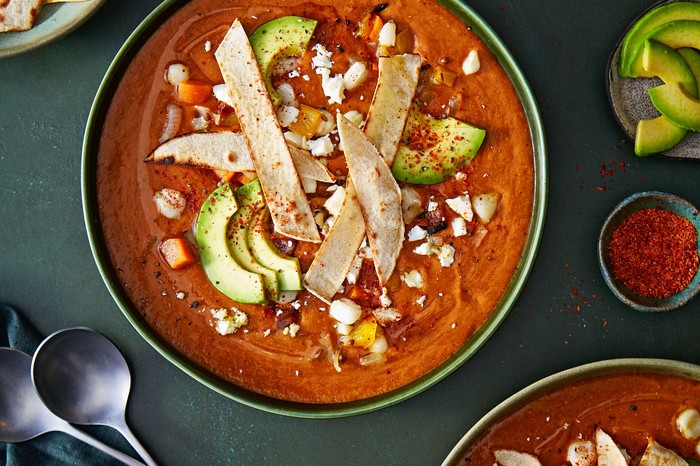 A bowl of red Mexican soup topped with tortilla strips