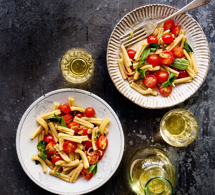 Two bowls of tomato pasta with glasses of white wine