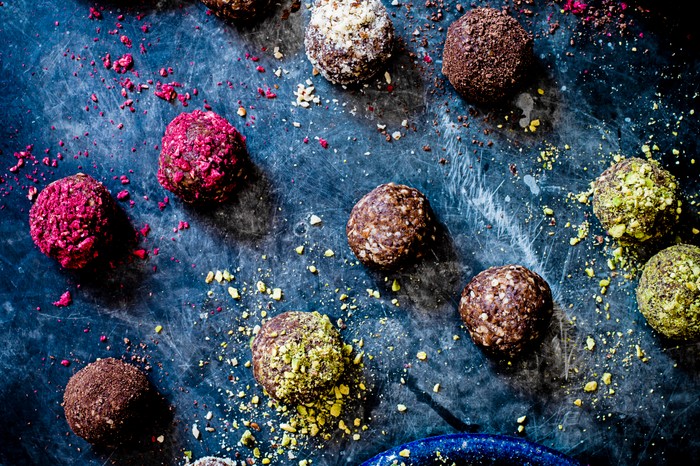 Coconut butter, date and cranberry energy balls with two plates of pistachios and dried cranberries on the side