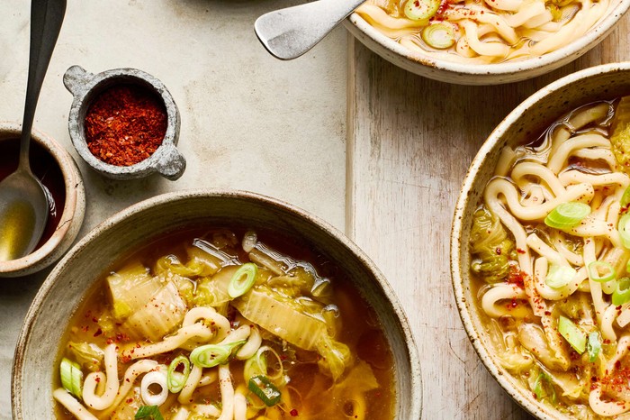 Three bowls of noodle soup with spices on the side
