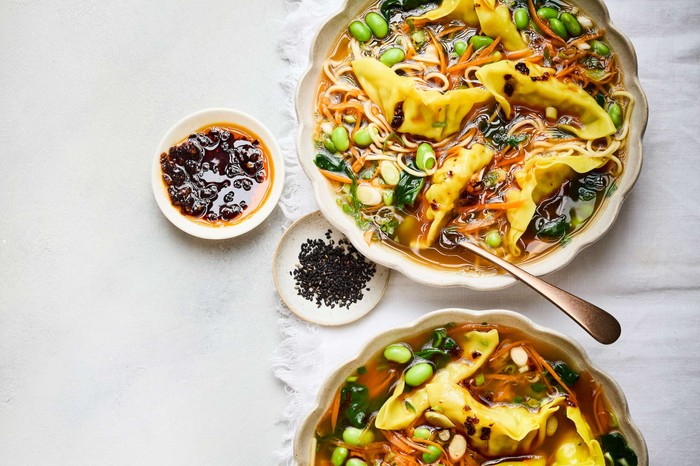 Two bowls of broth with dipping sauces on the side