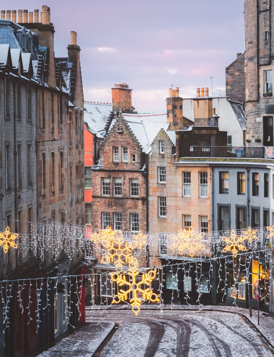 Christmas decorations and the colourful shopfronts of Victoria Street in Edinburgh's old town on a winter morning after a fresh overnight snowfall.