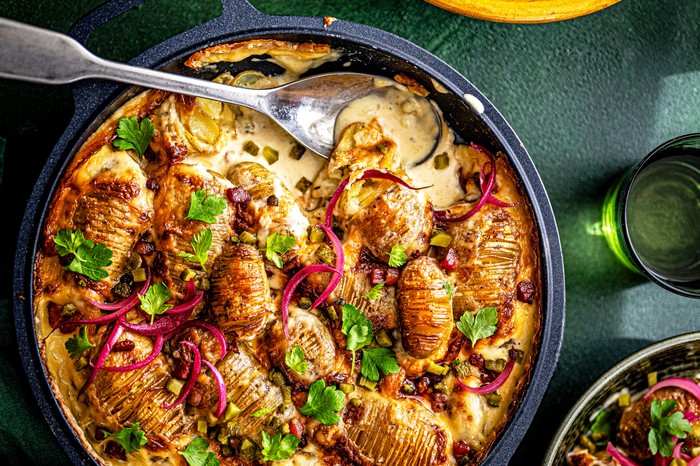 A hasselback tartiflette with pickle salad, with a spoon in it