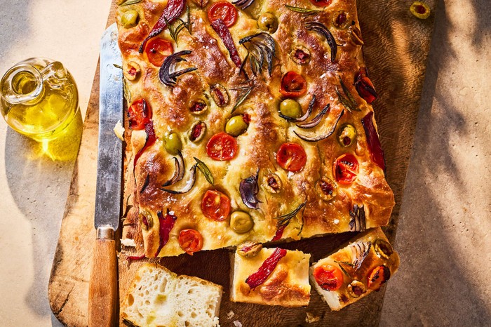 A whole focaccia topped with olives with one slice taken out of it