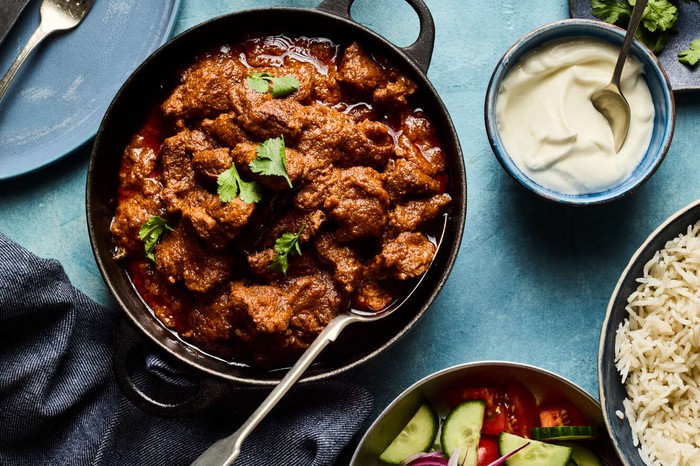 A mutton curry with rice and dips on the side