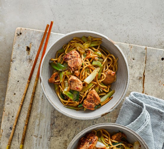 A bowl of chicken chow mein next to some chopsticks on a tabletop