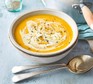 Carrot and parsnip soup in a white bowl next to spoon