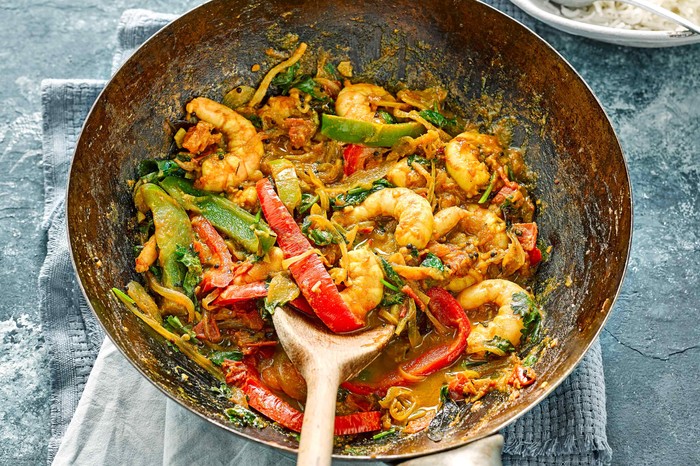 A silver wok is filled with prawns, chopped peppers and green vegetables