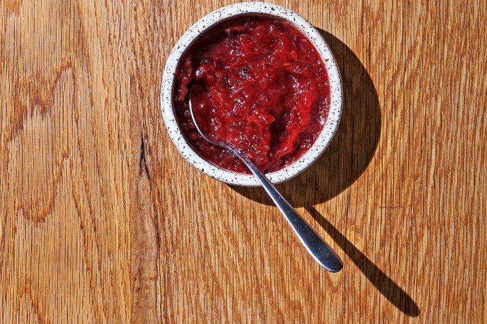 A small speckled bowl filled with dark red cranberry sauce with a metal spoon in the bowl