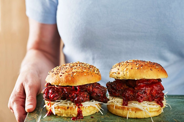 Someone holding a board with two chicken burgers on it