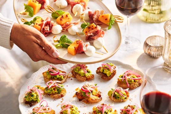 Someone holding a serving plate full of melon skewers