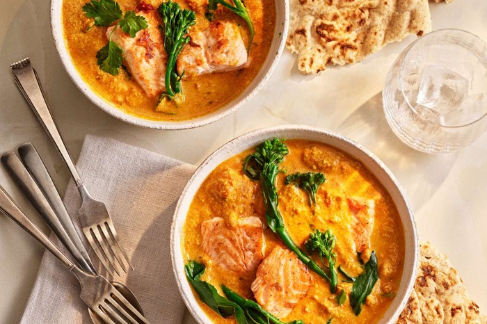Two bowls of salmon curry with cutlery on the side