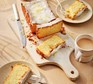 A lemon loaf cake with one slice cut off and cups of tea on the side