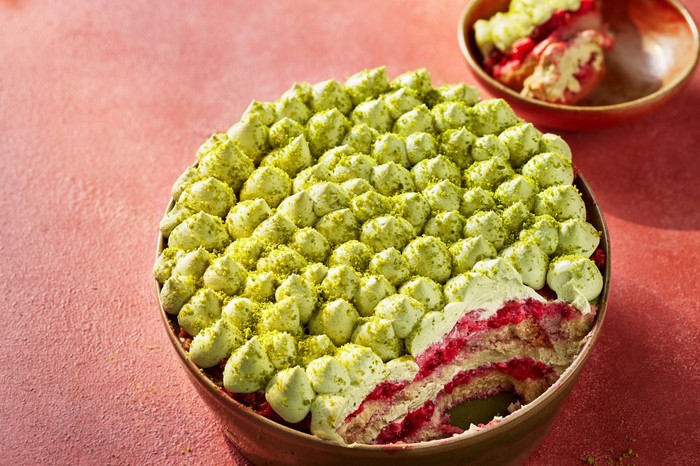 A whole pistachio and raspberry tiramisu with a slice taken out of it