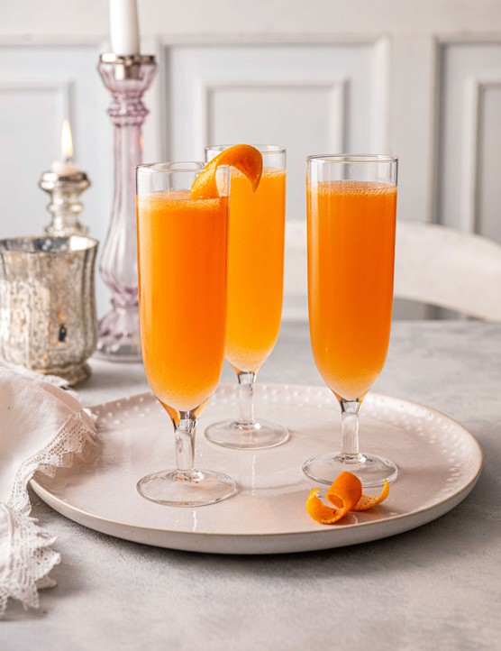 Three orange-coloured cocktails in champagne flutes