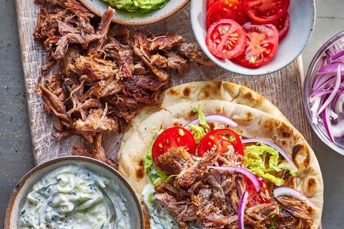 Flatbreads topped with pork gyros, tomatoes, red onion, lettuce. Next to a bowl of tzatziki