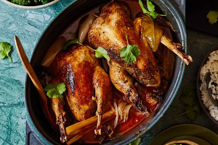 A Pot-roast red curry pheasant i a cast iron pot next to a bowl of broccoli