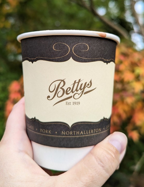 Bettys hot chocolate in a takeaway cup against autumnal trees