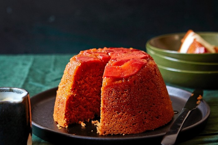 A steamed quince pudding on a black plate on a green linen table cloth