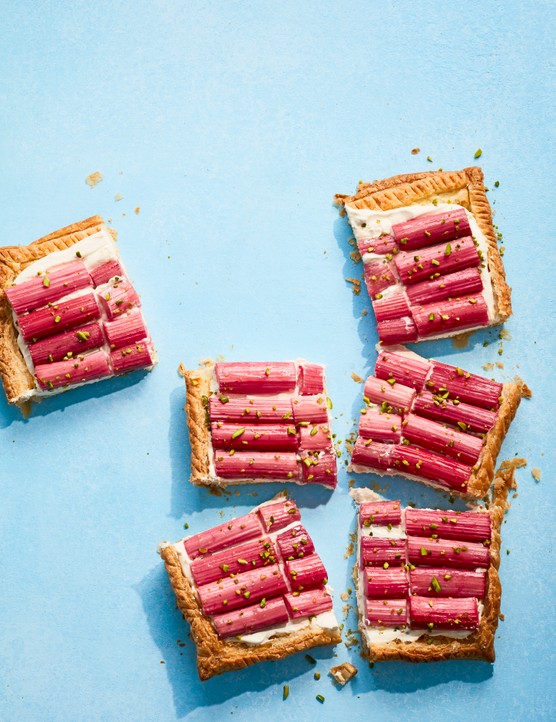 A rectangular puff pastry tart cut into squares and fllled with chopped rhubarb, on a blue background