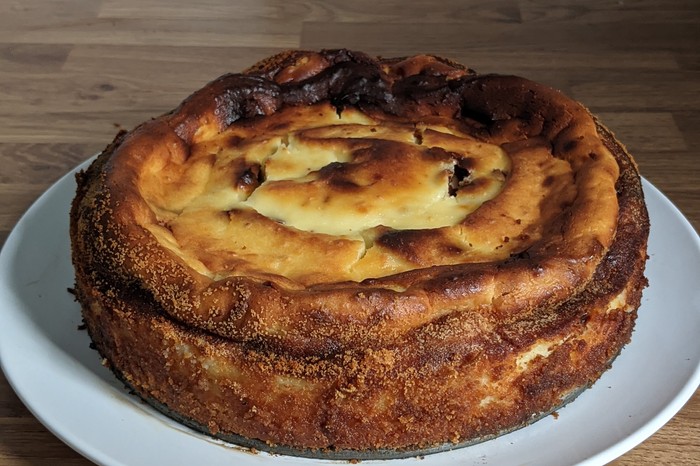 A golden ricotta cake on a white plate, sat on a wooden worktop