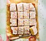 A school cake topped with icing and sprinkles cut into squares on a sheet of brown baking parchment
