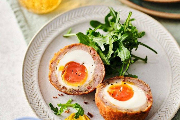 A homemade Italian sausage scotch egg cut in half with salad on the side