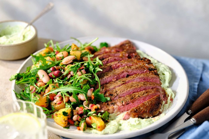 A plate of sliced steak with bean salad on the side
