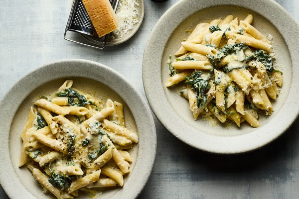 Two bowls of spinach pasta next to parmesan cheese