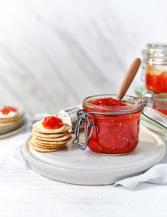 A jar of tomato jam with a stack of crackers next to it