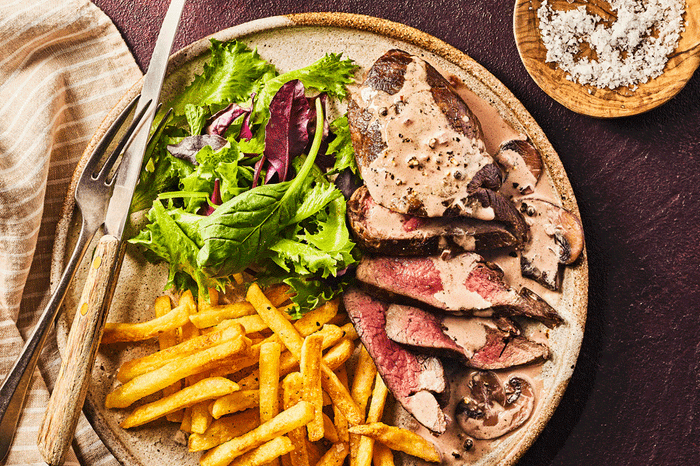 Slices of venison on a plate with chips, salad and mushroom peppercorn sauce