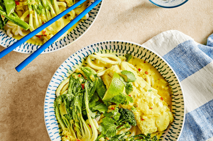 Two bowls of spiced cod in a creamy broth with green vegetables
