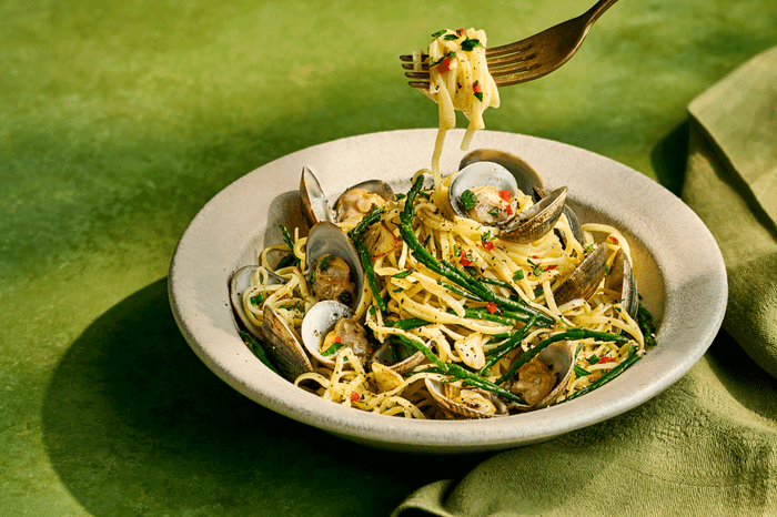 Tagliolini alle vongole in a bowl with a fork and a green background